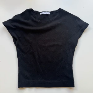 Svart topp från Zara - En enkel svart topp från Zara med rund halsringning och korta ärmar. Modellen är tight och passar perfekt till jeans eller kjol. Tillverkad i mjuk bomull som känns skön mot huden.