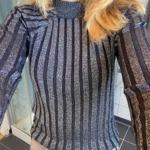 Glittrig randig tröja från Lindex - Glittrig tröja från Lindex i svart och silver med vertikala ränder. Tröjan har lång ärm och lite högre hals.