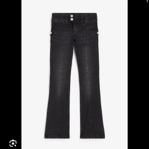Svarta bootcut jeans med fickor - Säljer ett par svarta bootcut jeans med två knappar i midjan och snygga fickor med lock på sidorna. Jeansen har markerad söm längs benen och sitter tajt upptill men släpper ut vid bensluten. Perfekta för dig som gillar en retro vibe. köpte på h&m barn för länge sen och dom finns inte att köpa längre. storlek 158