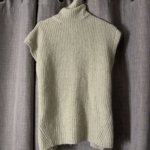 Ribbstickad beige väst med polokrage - Om du är intresserad skriv inann du köper! Ribbstickad väst i beige med hög polokrage och ärmlös design. Västen har en öppen ryggdetalj som ger en cool twist. Perfekt att slänga över en skjorta eller t-shirt för en trendig lager-på-lager-look.