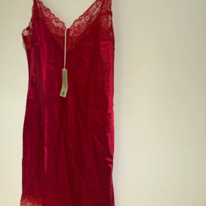 Röd spetsklänning i silke , stl S - Supersnygg röd klänning i 100% silke  med spetsdetaljer vid urringningen och nederkanten. Klänningen har smala axelband och en figurnära passform som ger en elegant siluett. Perfekt för dig som vill sticka ut med en färgstark look.