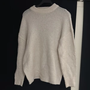 Vit stickad tröja från 157 - Mysig vit stickad tröja från 157 med relaxed fit och ribbade muddar vid ärmslut och hals. Perfekt för lager-på-lager och chill dagar. Tröjan har en enkel design med rund hals och långa ärmar, vilket gör den superenkel att styla till allt.