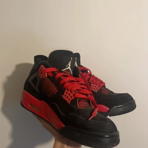 Nike Air Jordan 4 svart/röd sneakers - Säljer ett par Nike Air Jordan 4 sneakers i svart och rött med klassisk Jumpman-logga på plösen och hälen. Skorna har röda snören, meshdetaljer och en robust sula. Perfekta för dig som gillar streetstyle och vill sticka ut med en ikonisk modell, använt 2 gånger. 
