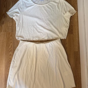 Två delat set i ljusgult - Supersött set i ljustgult ribbat tyg, tshirt med korta ärmar och kortkjol från Bubbleroom i storlek XL. Kjolen har en mjuk och stretchig känsla, med diskreta vertikala ränder och elastisk midja. Perfekt för dig som gillar en clean och enkel stil med lite edge.