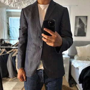 Mörkblå kavaj från Tiger of Sweden - Snygg mörkblå kavaj från Tiger of Sweden i klassisk modell med två knappar framtill och smala slag. Tillverkad i ullblandning med en stilren, lätt glansig finish. Perfekt för dig som vill ha en dressad look med modern passform.