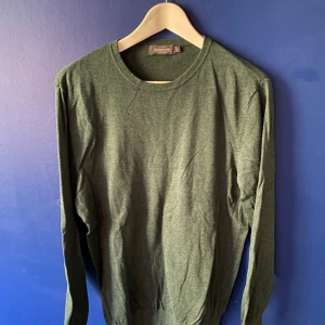 Mörkgrön bomullströja från Dressmann - En stilren mörkgrön tröja från Dressmann i mjuk pima bomull. Tröjan har rund halsringning, långa ärmar och ribbade muddar vid ärmslut och nederkant. Perfekt för lager-på-lager och enkel att matcha med jeans eller chinos.