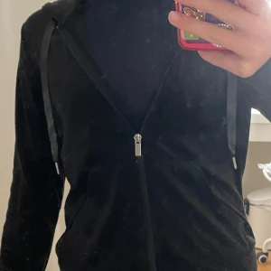 Svart tröja från Gina Tricot - Svart tröja från Gina Tricot i mjuk velourkänsla. Jackan har dragkedja framtill, huva med snören och fickor på sidorna.