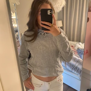 Grå hoodie med snörning - En basic grå hoodie med huva och snörning framtill. Tröjan har en stor magficka och långa ärmar. Perfekt för chill dagar eller när du vill ha något bekvämt och enkelt. Passformen är normal och materialet känns mjukt mot huden.