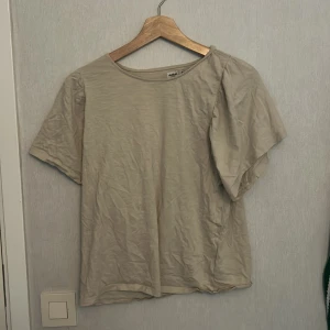 Beige kortärmad topp från Dobber - Enkel och stilren beige topp från Dobber i mjuk bomull. Modellen har korta ärmar med lätt puff vid axeln och rund halsringning. Perfekt att matcha med jeans eller kjol för en clean look.