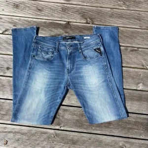 Replay Anbass ljusblå jeans 30/32 - Snygga Replay Anbass jeans i ljusblå tvätt med klassisk femficksdesign och diskreta slitningar. Jeansen har raka ben och normal passform, tillverkade i mjukt bomullsmaterial med lite stretch för extra komfort. Perfekta för en avslappnad och trendig look.