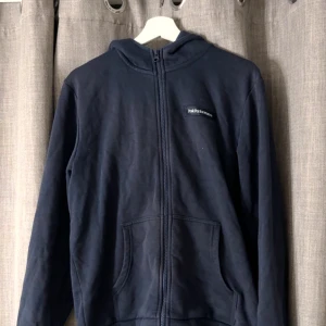 Mörkblå hoodie från Peak Performance - Snygg mörkblå hoodie från Peak Performance med dragkedja och huva. Tröjan har två stora fickor framtill och diskret logga på bröstet. 