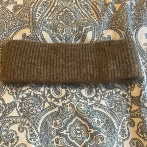 Brun stickad pannband i ullmix - Mysigt brunt stickat pannband i ribbad design. Tillverkat i en mjuk mix av ull, alpacka, akryl och polyamid som håller dig varm under kyliga dagar, jätteskönt verkligen och håller huvudet varmt, använd några få gånger, köpt från Ullared minns inte för hur mycket 