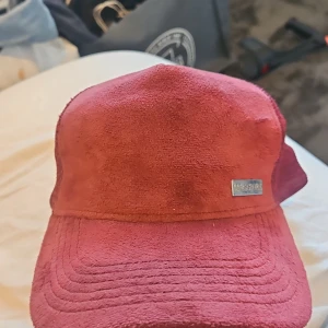 Vinröd keps från Maggiore - Snygg vinröd keps från Maggiore med mjuk mocka framtill och mesh baktill för extra ventilation. Justerbar passform med plastspänne. Perfekt accessoar för en cool och avslappnad stil.