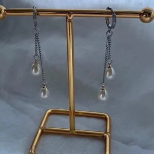 Silverörhängen med hängande pärlor - Snygga örhängen i silverfärg med dubbla kedjor och droppformade vita pärlor. Kedjorna ger ett coolt och elegant intryck och pärlorna hänger fint och rör sig när du går. Perfekta för att lyfta din outfit med en trendig touch.