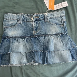 Jeanskjol med volanger från Gina Tricot - Supersnygg jeanskjol från Gina Tricot i mellanblå denim. Kjolen har låg midja, och volnger nedtill. Jag säljer den då den är för liten för mig.
