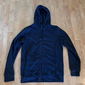 Mörkblå zip-up från Dressmann  - Mörkblå zip-up från Dressmann i storlek S. Tröjan har dragkedja framtill, två sidofickor och en skön huva. Tillverkad i mjukt material som passar perfekt för chill dagar. 