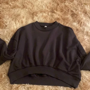 Svart croppad sweatshirt H&M XS - Svart croppad sweatshirt från H&M Basic i storlek XS. Tröjan har rund halsringning, långa ärmar och breda muddar vid ärmslut och nederkant. Perfekt för en chill och avslappnad stil.