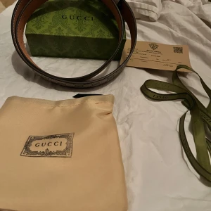 Gucci GG Supreme bälte med silverdetalj - Snyggt Gucci-bälte i klassiskt GG Supreme-mönster med beige och grå toner. Bältet har en stor silverfärgad GG-logga som spänne och är gjort i skinn med canvas-yttersida. Kommer med originalbox, dustbag och band. Perfekt accessoar för att lyfta din outfit. Köpte för runt 400euro och den är äkta direkt från Italien.