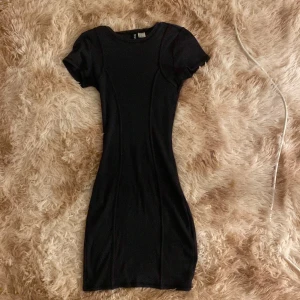 Svart tight kortklänning H&M Divided - En svart, tight och enkel kortklänning från H&M Divided. Klänningen har korta ärmar och rund halsringning, med en figurnära passform som framhäver siluetten. Perfekt för dig som gillar minimalistisk och stilren look.