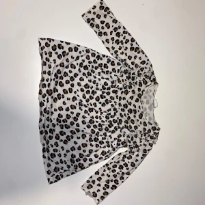 Leopardmönstrad klänning från H&M - Supersöt kort klänning från H&M med leopardmönster i svart och brunt på ljus botten. Långärmad modell i mjuk bomull, perfekt för dig som gillar djurmönster och vill sticka ut lite extra.