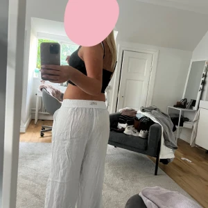 Vita linnebyxor med snörning - Säljer ett par vita linnebyxor med avslappnad passform och resår i midjan. Byxorna har snörning framtill och är tillverkade i ett lätt och luftigt linnematerial, perfekta för varma dagar. De har raka ben och en enkel, stilren look.