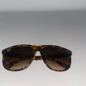 Ray-Ban solglasögon  - Snygga Ray-Ban solglasögon med leopardmönstrad båge i bruna och gula toner. Klassisk fyrkantig form och bruna tonade glas. Perfekt accessoar för att lyfta din stil med en cool retrovibe.