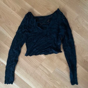 Svart spetsig croppad långärmad topp - Säljer en svart croppad topp med lång ärm i genombruten spets och blommigt mönster. Toppen har v-ringning och är riktigt snygg till höga jeans eller kjol. Perfekt för dig som gillar detaljer och vill sticka ut lite extra.