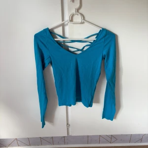 Turkos långärmad topp med snörning - Snygg turkos långärmad topp med v-ringning och cool snörningsdetalj över bröstet. Toppen är figurnära och gjord i mjuk bomull, perfekt att styla med jeans eller kjol för en trendig look.
