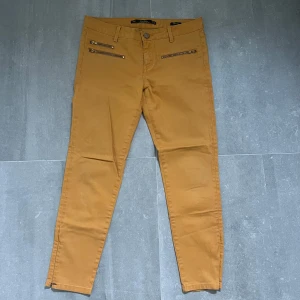 Mustardfärgade skinny byxor med dragkedjor - Snygga senapsgula byxor i skinny fit. Byxorna har flera coola dragkedjor framtill och vid benslut, samt bälteshällor och bakfickor. Tillverkade i mjuk bomullsblandning för en bekväm känsla.