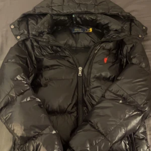 Ralph Lauren jacka  - Säljer en svart pufferjacka från Polo Ralph Lauren med avtagbar huva och dragkedja framtill. Jackan har en röd broderad logga på bröstet och flera praktiska fickor. Perfekt för kalla dagar och hösten💫knappast använd, går att diskutera pris !!