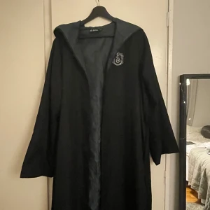 Slytherin rock från Harry Potter S-M - Säljer en svart lång rock med huva från Harry Potter, Slytherin. Rocken har Slytherin-emblem broderat på bröstet och är fodrad med mörkgrönt tyg. Är i bra skick och är bra kvalitet. Från emp of Sweden. 