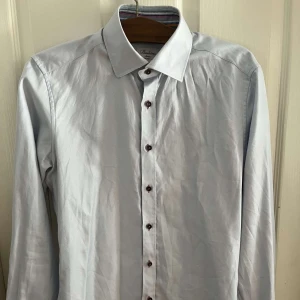 Ljusblå slim fit skjorta Stenströms - Snygg ljusblå skjorta från Stenströms i slim fit-modell. Skjortan är tillverkad i exklusiv tvåfaldig bomull och har klassisk krage samt mörka knappar framtill. Perfekt för dig som gillar stilrena och fräscha plagg.