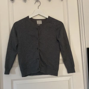 Mörkgrå kofta från Zara Knitwear - En stilren mörkgrå kofta från Zara Knitwear med rund halsringning och knappar framtill. Långärmad och i mjukt stickat material, perfekt att slänga över en t-shirt eller topp. Enkel och clean look som funkar till det mesta.