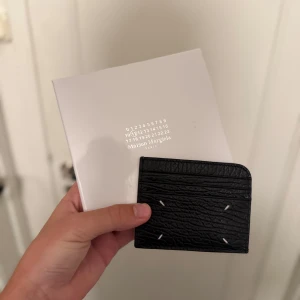 Maison Margiela korthållare - Säljer en svart korthållare från Maison Margiela i skinn. Den har flera kortfack, vita signatursömmar och Maison Margielas ikoniska logga tryckt på framsidan. Kommer med originalbox och dustbag.