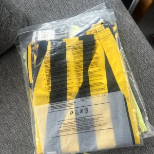 Fenerbahce randig matchtröja Adidas - Fet Fenerbahce fotbollströja från Adidas med klassiska gula och mörkblå vertikala ränder. Tröjan har klubbmärket på bröstet, Adidas-logga och sponsortryck. Snygga detaljer vid kragen och axlarna. Perfekt för dig som vill sticka ut på läktaren eller planen.