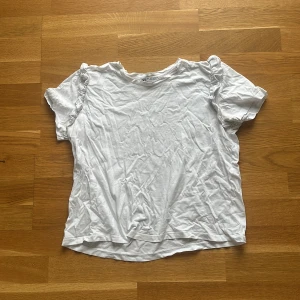 Vit volangärmad topp från Zara - Säljer en vit topp från Zara med korta ärmar och volangdetaljer på axlarna. T-shirten har en klassisk rund halsringning och är gjord i mjuk bomull, perfekt för en clean och enkel look.