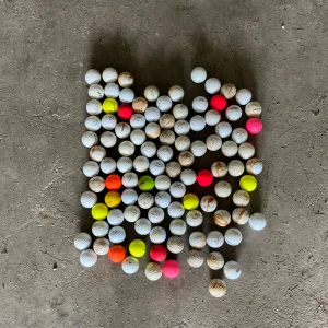 30 callaway - Bilden visar ett stort antal golfbollar i olika färger, inklusive vita, gula, orangea och rosa. Golfbollarna är använda och har varierande grad av smuts och slitage. Ingen bok syns på bilden.