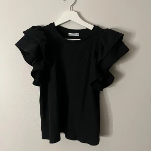 Svart topp med volangdetaljer - Snygg svart topp från Zara med volangdetaljer på axlarna. Säljer denna topp pga att den har blivit för liten🌸