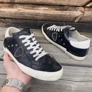 Philippe Model skor - Snygga svarta sneakers från Philippe Model med vita detaljer och snörning. Skorna har en klassisk design med en vit sula och är perfekta för en stilren look. Har en liten defekt bak, därav priset