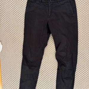 Svarta chinos från J.Lindeberg - Snygga svarta chinos med normal passform. Storlek 32/32. Finns en liten fläck på framsidan som no går bort med vanish.