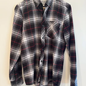 Flanellskjorta från Carhartt - Snygg rutig skjorta från Carhartt i svart, vit och röd. Skjortan är i bra skick utan några skador eller fläckar. Står att den är xs men passar lite större