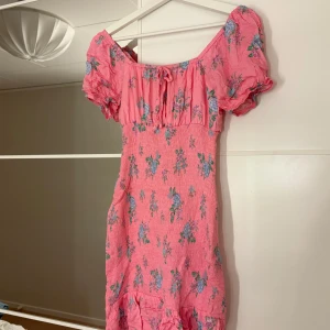 Rosa blommig klänning - Charmig rosa klänning med blommigt mönster i blått och grönt. Klänningen har korta puffärmar och en söt volangdetalj längst ner. Hör av er vid funderingar eller om ni vill ha bilder med hur plagget sitter på mig. Titta gärna in mina andra plagg!