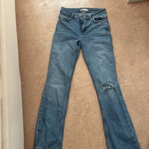 Blå jeans med slitningar - Snygga blå jeans med slitningar på knäna. De har en klassisk femficksdesign och knappgylf. Perfekta för en avslappnad stil.