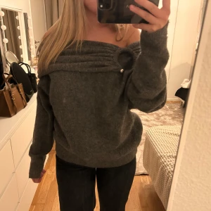 Grå offshoulder tröja med detalj - Säljer en snygg grå offshoulder tröja med unika pärldetaljer vid halsen. Tröjan har långa ärmar och en lös passform som ger en avslappnad look. Perfekt för kyligare dagar.