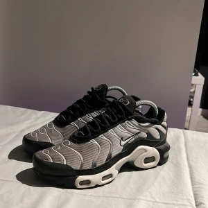Nike sneakers i svart och grått - Snygga Nike sneakers i svart och grått med vågigt mönster och vit sula. Skorna har en sportig design med synlig Air-dämpning i hälen. Har bara använt dem några gånger innan dem blev för små. Har tyvärr inte låda.