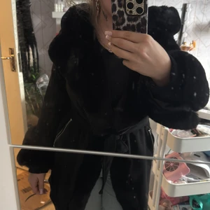 Svart pälsjacka från Garoff - Säljer en elegant svart pälsjacka från Garoff. Jackan har en lyxig känsla med mjuk päls och ett knytbälte i midjan. Den har långa ärmar och en stor krage som ger extra värme och stil. Perfekt för kyliga dagar. Storlek M inga skador eller liknande.