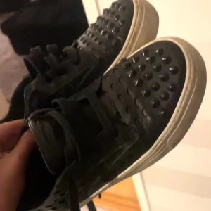 Svarta sneakers med nitar - Snygga svarta sneakers med nitar på ovansidan och en vit sula. Skorna har snörning och en cool design som sticker ut. Perfekta för att ge din outfit en edgy touch.