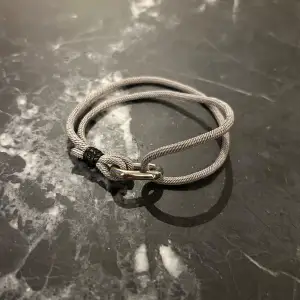 Justerbart grått armband med ett stilrent metallspänne. Armbandet har en enkel och modern design som passar till många olika stilar. Perfekt för både vardag och speciella tillfällen. 
