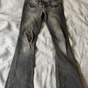 Grå bootcut jeans från Pussycat - Snygga grå bootcut jeans från Pussycat med låg midja och coola detaljer som dubbla knappar och framfickor med lock. Inga bakfickor. Midjemått 38-39cm (beroende på vilken knäppning) innerbenslängd 77cm. 