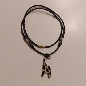 Svart halsband med giraffhänge - Unikt svart halsband med ett giraffformat hänge i svart och vitt. Halsbandet har små svarta pärlor och med ett snurr lås. Skriv om ni har någon fundering!✨️